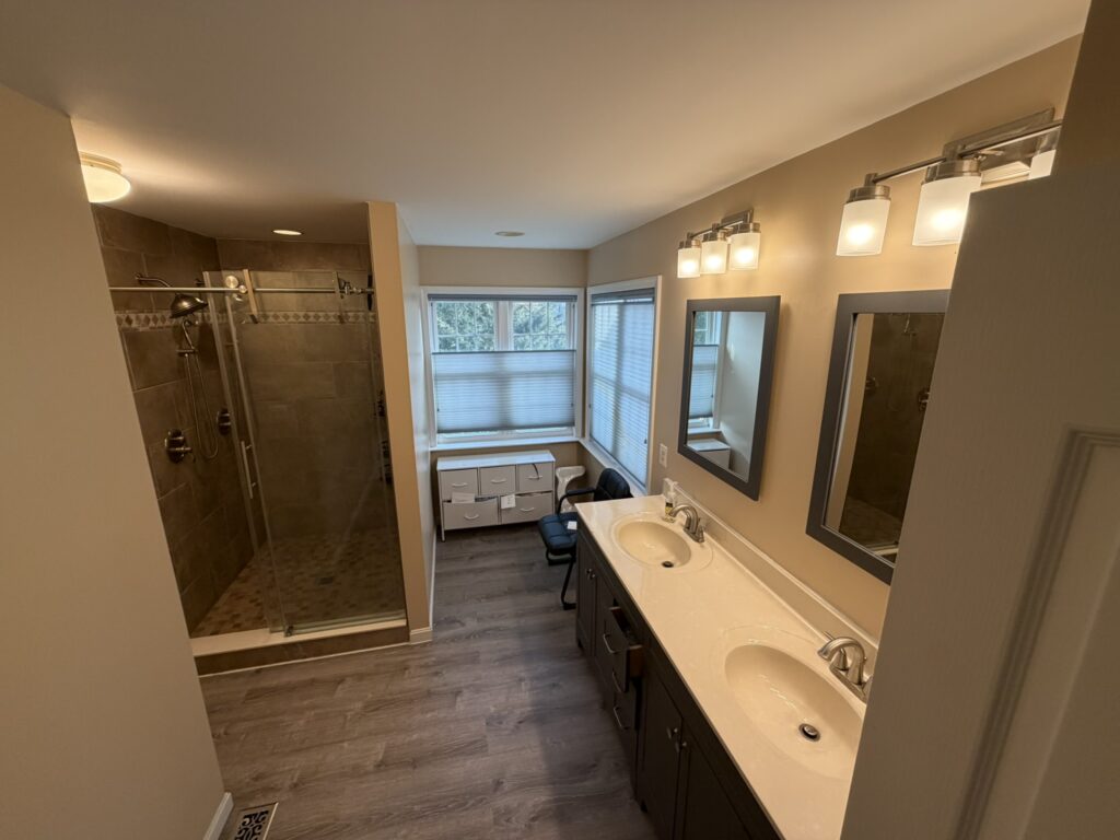 Modern bathroom with double vanity, glass walk-in shower, and large window with natural light.