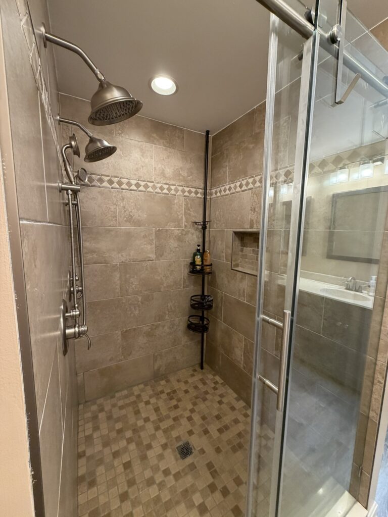 Tiled walk-in shower with glass door, four showerheads, and built-in niche shelf.