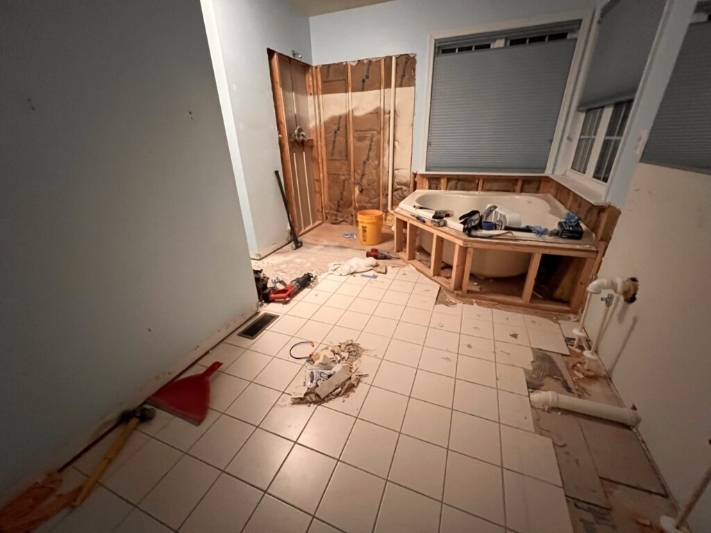 Bathroom demolition in progress with tub removed, walls opened, and subfloor exposed for full remodel