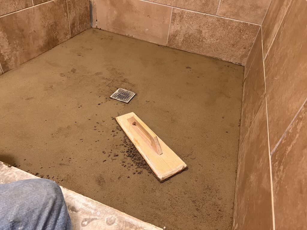 Custom shower pan mortar bed being formed and leveled with proper slope to drain during bathroom remodel